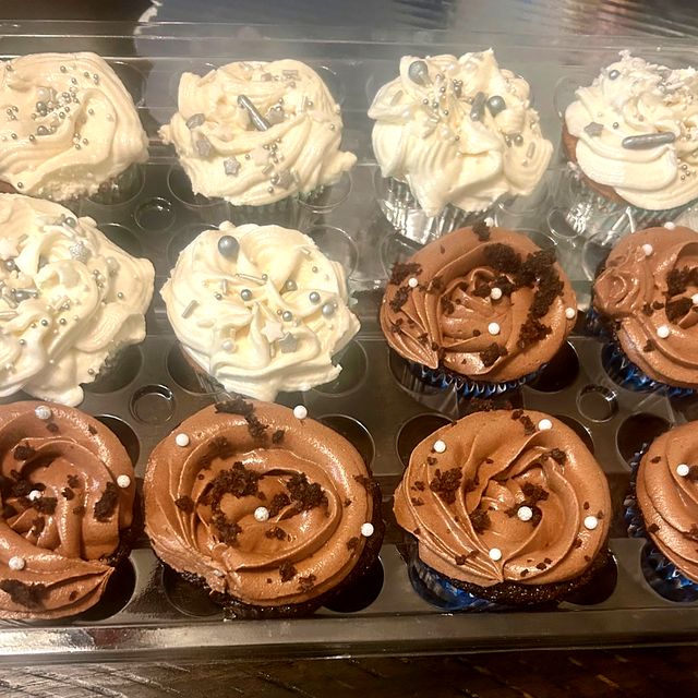 A dozen vanilla and chocolate cupcakes with swirled frosting and pearl sprinkles