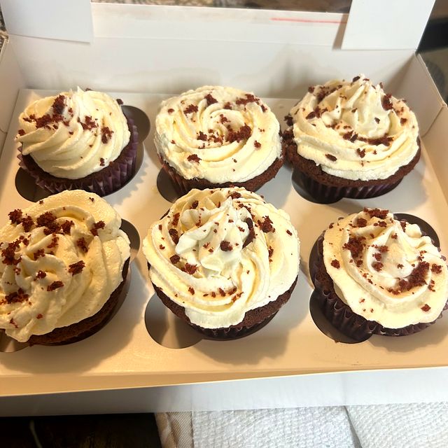 A box of chocolate cupcakes with cream cheese frosting and red velvet crumbs