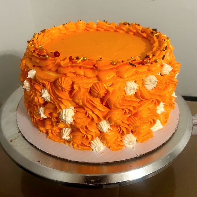 Two-layer custom cake with orange buttercream and white piped flowers