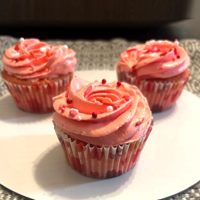 Three strawberry cupcakes with pink swirled frosting and sprinkles